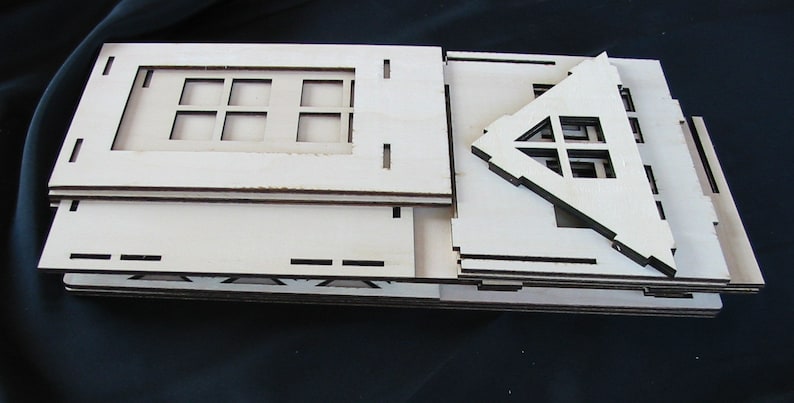 K&ouml;nnte beinhalten: Ein Satz unfertiger Holzst&uuml;cke zum Bau eines kleinen Hausmodells. Die Teile sind gestapelt und beinhalten ein Dach, W&auml;nde und Fenster.