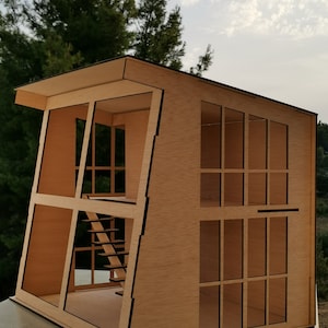 K&ouml;nnte beinhalten: Ein Holzmodell eines modernen Hauses mit Flachdach und gro&szlig;en Fenstern. Das Haus ist aus Sperrholz gefertigt und hat eine Treppe im Inneren. Das Modell ist unvollendet und hat eine nat&uuml;rliche Holzfarbe.