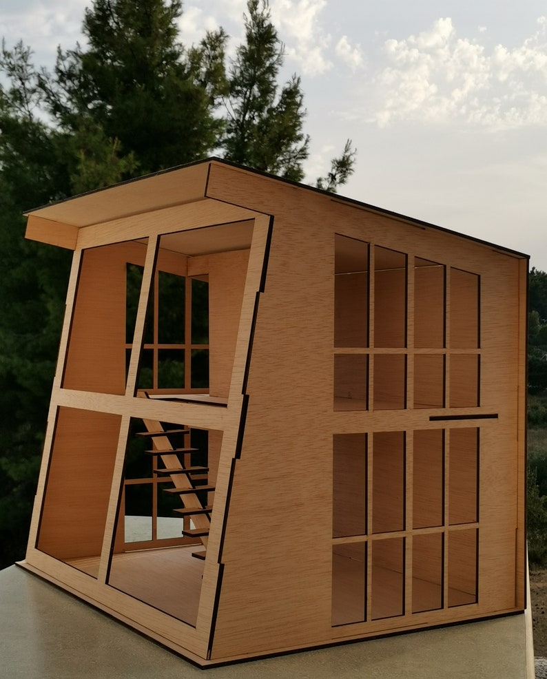 K&ouml;nnte beinhalten: Ein Holzmodell eines modernen Hauses mit Flachdach und gro&szlig;en Fenstern. Das Haus ist aus Sperrholz gefertigt und hat eine Treppe im Inneren. Das Modell ist unvollendet und hat eine nat&uuml;rliche Holzfarbe.
