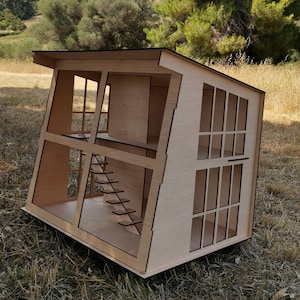 K&ouml;nnte beinhalten: Ein Holzmodell eines Puppenhauses mit einem schr&auml;gen Dach und mehreren Fenstern. Das Puppenhaus ist aus hellbraunem Holz gefertigt und hat eine Treppe im Inneren.