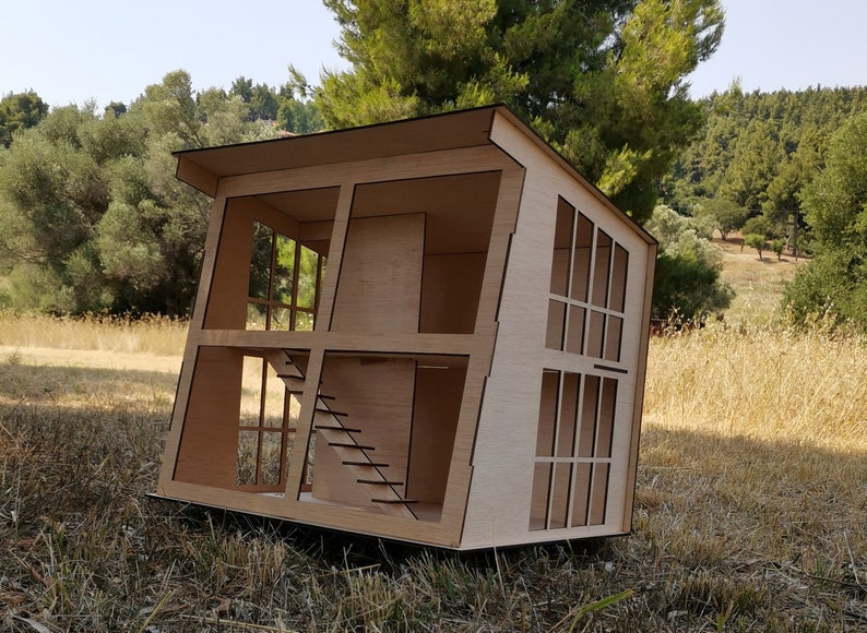 K&ouml;nnte beinhalten: Ein Holzmodell eines Hauses mit einem schr&auml;gen Dach und gro&szlig;en Fenstern. Das Haus ist aus hellbraunem Holz gefertigt und hat ein schlichtes Design.