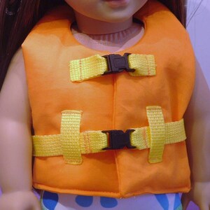 May include: Orange life vest with yellow straps and black buckles. The vest is designed for a doll.