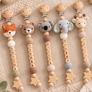 Peut inclure: Cinq attaches-sucettes personnalisées avec des têtes d'animaux en crochet : renard, ours, koala, éléphant et girafe. Chaque attache comporte des perles en bois, certaines avec les prénoms Sofia, Liam, Dylan, Ben et Amelia, et une étoile.