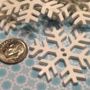 May include: White plastic snowflake ornaments, approximately the size of a US dime.