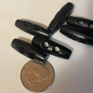 May include: Six black wooden toggle buttons with two holes each. The buttons are arranged in a pile on a white surface.