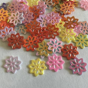 May include: Assortment of colorful, iridescent, laser-cut flower shaped embellishments. The flowers are made of a thin, shiny material and have a delicate, intricate design.