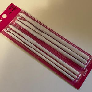 May include: A set of five white Susan Bates Luxite crochet hooks in a pink and white plastic retail package. The packaging displays the brand name and size range from 3.75 mm to 6.5 mm, corresponding to US sizes F-5 through K-10.5.