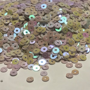 May include: A pile of iridescent white, pink, and yellow sequins in a round shape.