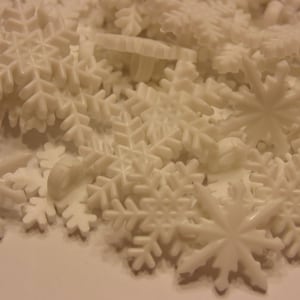May include: A collection of white plastic snowflake-shaped buttons, each featuring a six-pointed star design with intricate branching arms and a small loop on the back for attachment, scattered together in a dense, overlapping pile.