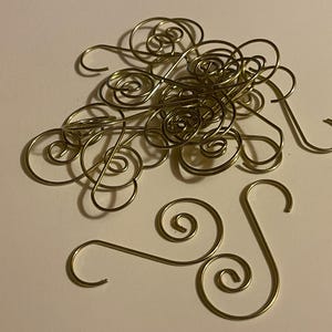 May include: A collection of gold-toned metal ornament hooks, each featuring a double-ended spiral design. These wire hooks are shaped with a hook at each end, connected by a central S-curve, and are arranged in a loose pile with two separate hooks.