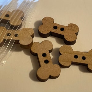 May include: Five wooden bone-shaped buttons with two holes each. The buttons are light brown and have a smooth finish.