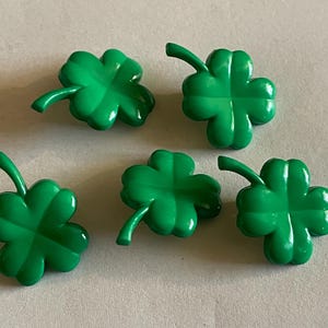 May include: Five bright green, plastic shamrock decorations. Each four-leaf clover has a stem and is set against a neutral background. These decorative shamrocks are ideal for St. Patrick's Day.