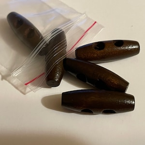 May include: Five brown wooden toggle buttons with two holes each. The buttons are in a clear plastic bag with a red zipper.
