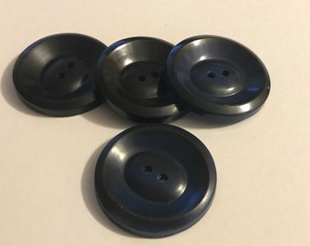 May include: Four large, black buttons with a two-hole design. The buttons have a slightly concave center and a raised outer rim. These buttons are suitable for various sewing projects.