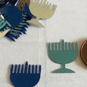 May include: Assortment of blue and green menorah cutouts, some with a silver finish. The menorahs are in various sizes and shapes. There is also a penny coin in the image.