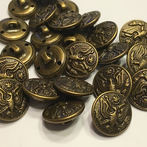 May include: A collection of round, antique brass-toned metal buttons, each featuring a detailed embossed eagle design with wings spread, a sunburst motif above the head, and a small loop shank on the back for attachment to garments.