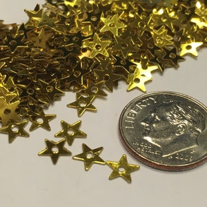 May include: A pile of gold star-shaped sequins, some of which are scattered around a US dime coin.