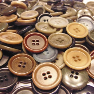 May include: A pile of various-sized buttons in shades of brown, tan, and gray. The buttons have four holes for sewing and are made of a smooth, glossy material. Some buttons have a slightly raised edge.