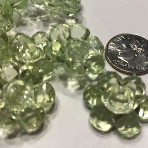 May include: A collection of light green, translucent, flower-shaped buttons with faceted edges. Each button features a central shank for attachment. A silver-colored United States dime is positioned next to the buttons to provide a scale reference.