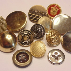 May include: A collection of assorted metal buttons in various gold and silver tones. The buttons feature diverse designs including smooth surfaces, textured patterns, embossed crests, a hand symbol with the text SASSON, and standard four-hole styles.
