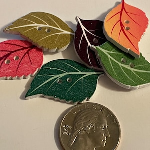 May include: Six wooden leaf-shaped buttons in various colors, including green, red, orange, brown, and purple. The buttons have two holes each and are approximately the size of a US quarter.