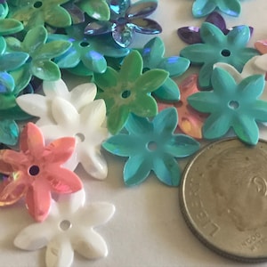 May include: A collection of flower-shaped sequins in various colors, including white, pink, green, and blue. A US dime is included for size reference. These sequins are ideal for crafts and embellishments.