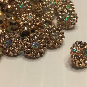May include: A pile of gold-colored buttons with iridescent glitter centers. The buttons are in the shape of a flower with multiple petals.