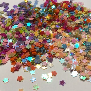 May include: A large pile of iridescent flower-shaped glitter in various pastel colors, including pink, blue, green, yellow, and orange.