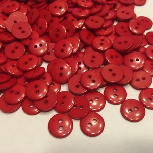 May include: A pile of red plastic buttons with two holes each. The buttons are round and have a glossy finish.