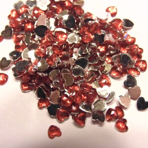 May include: A large pile of heart-shaped rhinestones in silver and red.