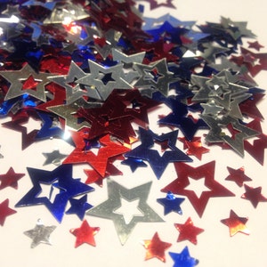May include: A pile of red, white, and blue star-shaped confetti. The stars are made of shiny, metallic paper.