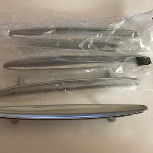 May include: A set of five silver-colored cabinet pulls, each with a curved, elongated design. The pulls are packaged in clear plastic, suggesting they are new and ready for installation. The hardware is likely for furniture or cabinetry.