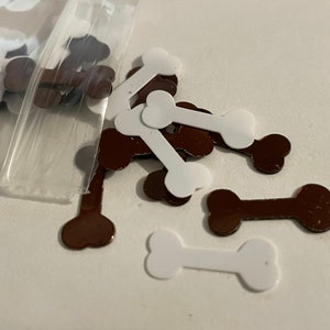 May include: A bag of white and brown bone-shaped confetti. The confetti is made of a shiny material and is perfect for adding a festive touch to any craft project.