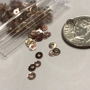 May include: A bag of small, gold and rose gold colored metal round sequins. The sequins are about the size of a dime.