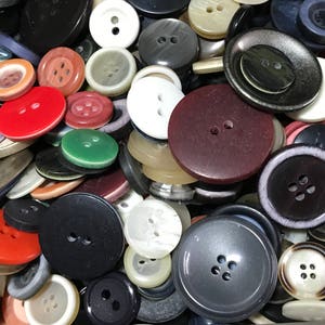 May include: A collection of various buttons in different colors and sizes. The buttons are round and have two or four holes for sewing. Colors include red, black, white, green, and gray. Some buttons have a glossy finish, while others are matte.