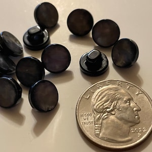 May include: A close-up of 11 black and iridescent round buttons, some with a black shank, next to a US quarter.