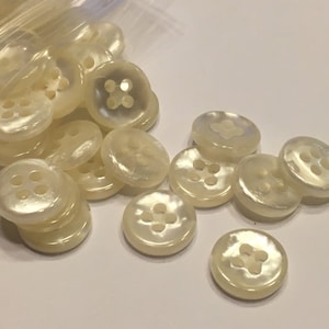 May include: A bag of white pearl buttons with four holes each. The buttons are round and have a smooth, shiny finish.
