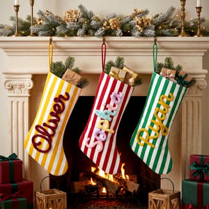 May include: Three Christmas stockings hanging from a mantel, each featuring vertical stripes and a personalised name in raised script lettering. The left stocking is yellow and white with the name Oliver, the centre is red and white with Sophia, and the right is green and white with Ryan.
