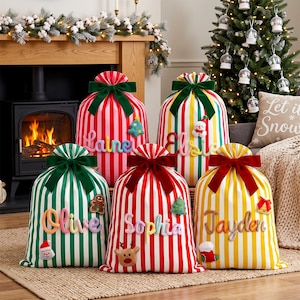 May include: Five fabric gift sacks with vertical stripes in red, green, and yellow, each tied with a velvet bow. The sacks feature personalised names in colourful rope lettering and small felt holiday appliques including a snowman, reindeer, and gingerbread man.