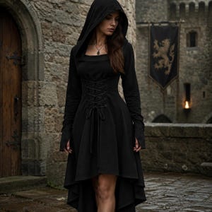 Könnte beinhalten: Ein schwarzes Kleid mit Kapuze, langen Ärmeln, eckigem Ausschnitt und einem geschnürten Korsett-Oberteil mit Bindeband vorne. Der Rock hat einen asymmetrischen Saum, der vorne kürzer und hinten länger ist, gefertigt aus einfarbigem Stoff.