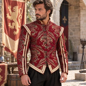 May include: A long-sleeved doublet featuring a deep red fabric with an intricate gold and dark green damask pattern. The garment has a high collar, a front button closure, and cream-colored trim along the shoulders, sleeves, and hem.
