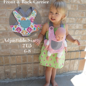 May include: A child wearing a green dress with pink cherries is carrying a doll in a pink and gray carrier. The carrier has adjustable straps and is labeled "Front & Back Carrier". The text "Adjustable Size: 2T-5 6-8" is also visible.