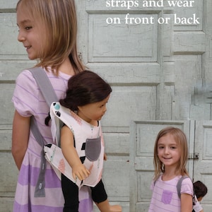 May include: Two children wearing purple and white striped dresses with adjustable straps. The straps can be worn on the front or back. One child is carrying a doll in a matching carrier.
