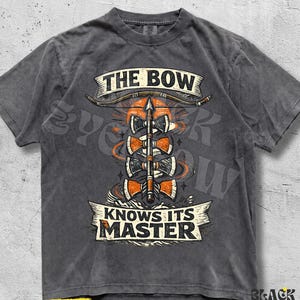 May include: A charcoal grey short-sleeve t-shirt featuring a graphic print of a bow and arrow with four axe heads stacked vertically. The text reads THE BOW at the top and KNOWS ITS MASTER at the bottom in a banner style with orange accents.