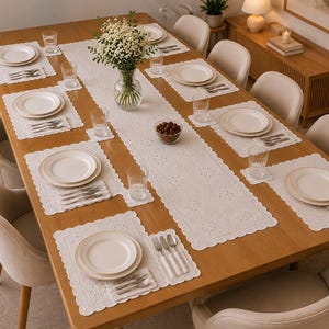 May include: A rectangular wooden dining table set for eight with white lace placemats and a matching table runner. Each place setting includes a white ceramic plate, a set of silverware, and a clear glass. A glass vase with white flowers sits in the center.
