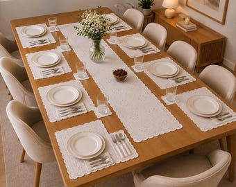 May include: A rectangular wooden dining table set for eight with white lace placemats and a matching table runner. Each place setting includes a white ceramic plate, a set of silverware, and a clear glass. A glass vase with white flowers sits in the center.