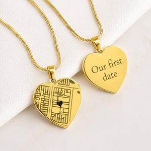Peut inclure: Deux pendentifs en forme de cœur de couleur dorée sur des chaînes assorties. L'un des pendentifs présente une gravure de plan de rue avec un petit cœur, tandis que l'autre porte l'inscription Our first date gravée en police serif.