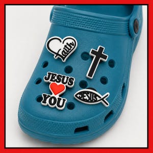May include: A teal clog shoe decorated with four charms: a white heart with the word Faith, a black cross, a white fish symbol with the word Jesus, and the words Jesus and You separated by a red heart. The charms are inserted into the shoe holes.