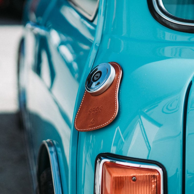 A close-up of a blue classic Mini Cooper featuring a personalized leather gas tank bib, showcasing a stylish and sophisticated automotive accessory