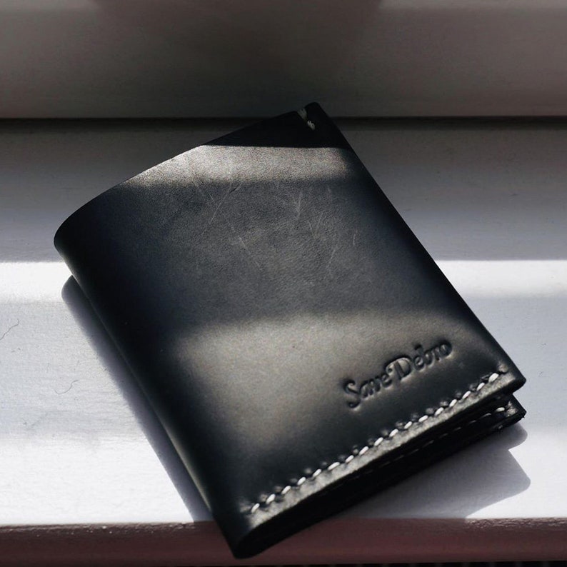 Personalized slim black leather wallet by Koncept Studios on window sill. Hand-stitched from Italian leather, with compartments for bills and cards.